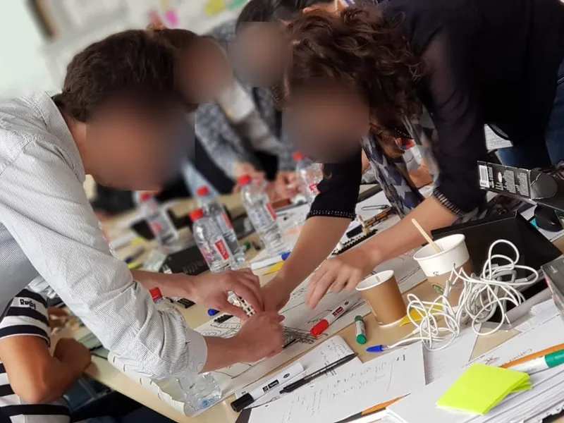 Atelier de prototypage autour d'une table : des participants construisent une maquette avec des briques et des post-its. Les visages sont floutés.