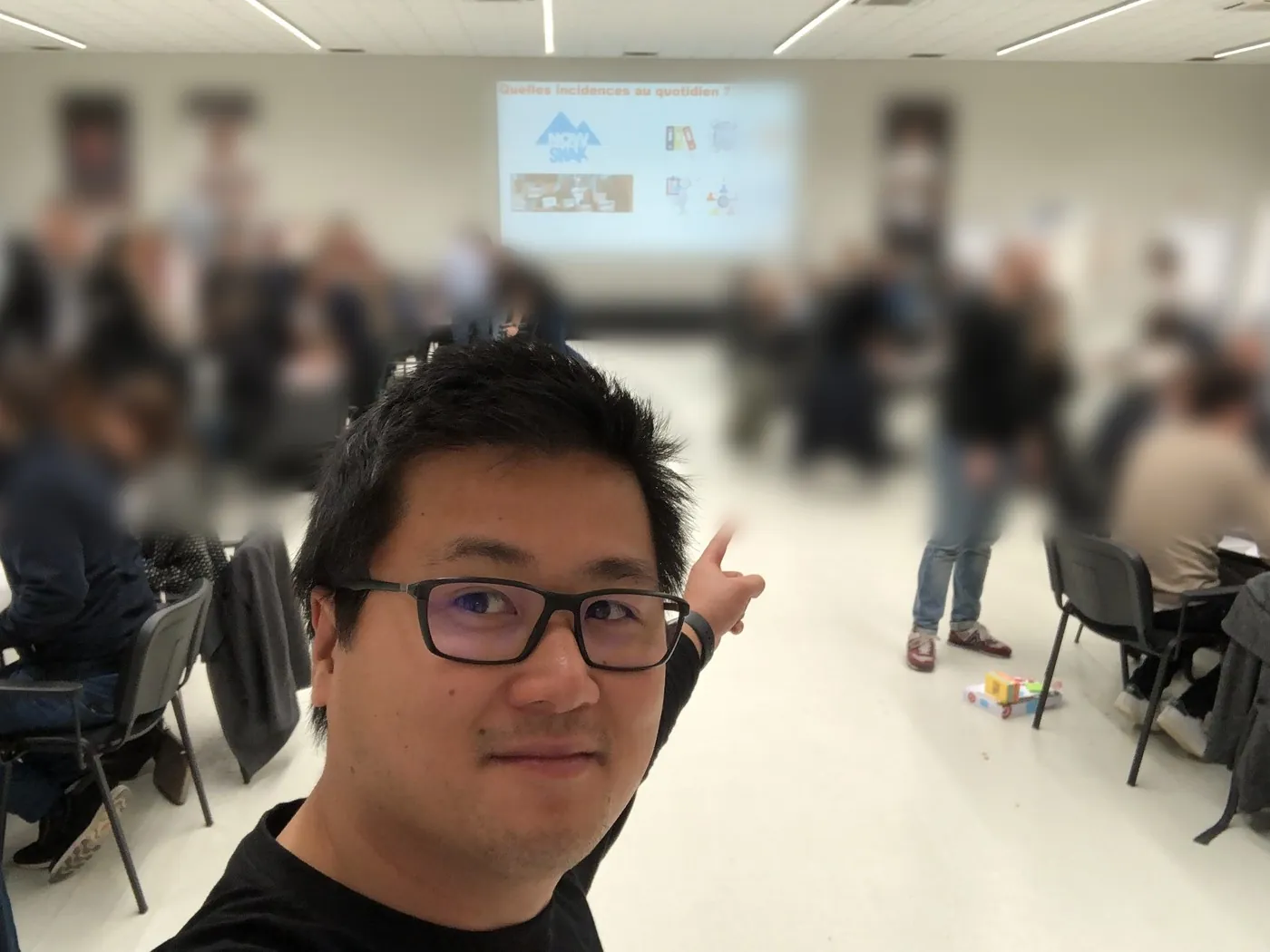 Stéphane Thanasack in front of a large off-site room running workshops; participants are blurred.