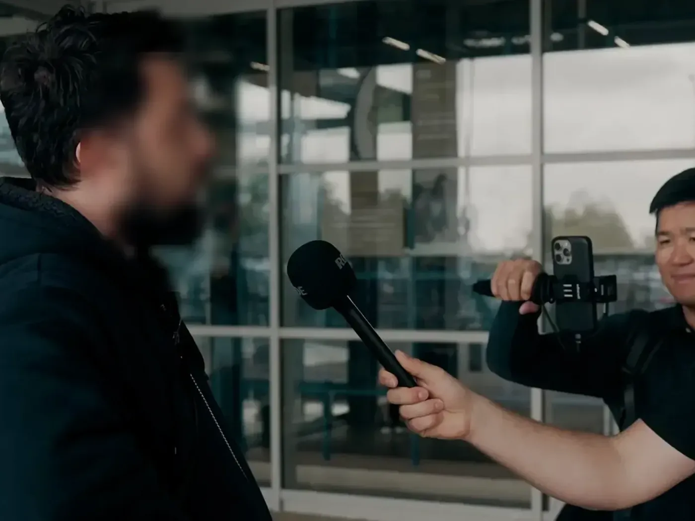 A customer interviewed with a microphone outside a store while Stéphane Thanasack films. The customer's face is blurred.