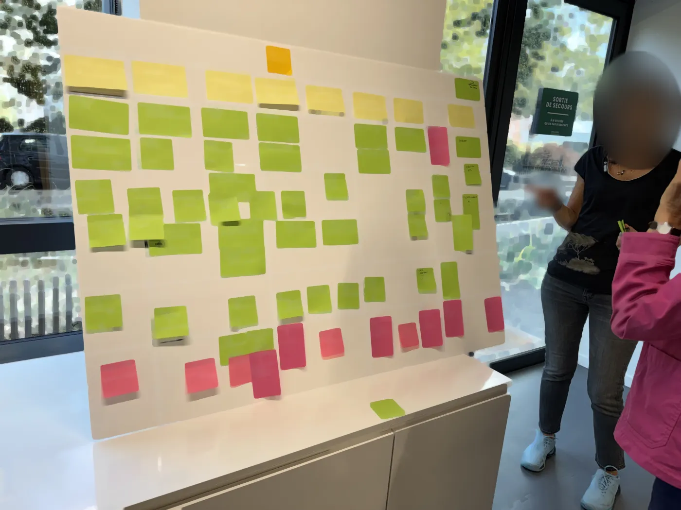 A facilitator in front of a board of green and pink sticky notes during a PI Planning